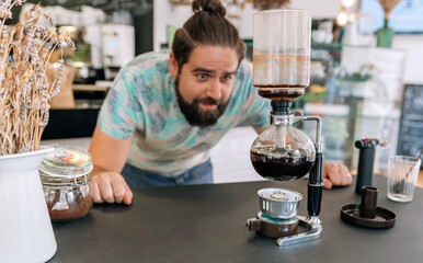 Focused barista expertly brews a specialty coffee in modern cafe. Setting highlights the art and precision involved in creating perfect cup of coffee. Selective focus on Japanese siphon coffee maker.