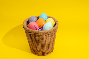 Multi colored easter eggs in a straw basket on a yellow background with copy space. Easter crafts...