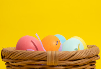 Extreme close up of multi colored easter eggs in a straw basket on a yellow background with copy space. Easter crafts concept