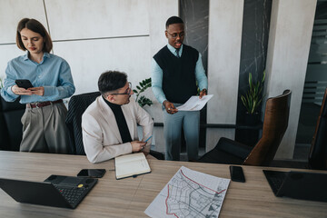 A multicultural group of business people engaged in a collaborative meeting in a modern office setting. Teamwork, technology use, and communication are evident in the workspace.
