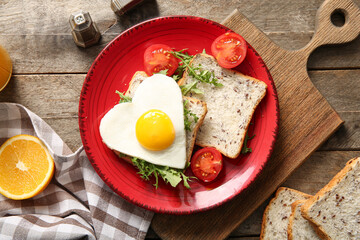 Plate with tasty fried egg, toasts, orange, tomatoes and arugula on wooden background