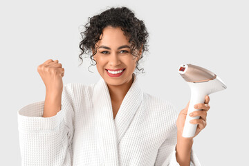 Beautiful happy African-American woman with photoepilator on white background