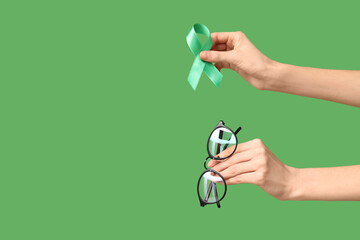 Female hands with ribbon and eyeglasses on green background. Glaucoma awareness concept