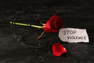 Paper with text STOP VIOLENCE, rose and barbed wire on dark background