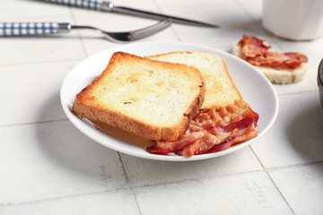 Plate with tasty bacon and toasts on light tile background, closeup