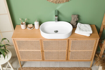 Modern sink with bath supplies on countertop near green wall in bathroom