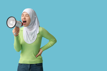Young Asian Muslim woman shouting into megaphone on blue background. National Be Heard Day