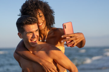 Interracial couple taking a joyful selfie on the beach during summer vacation