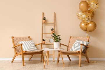 Beautiful golden air balloons with chairs and coffee table near beige wall at home