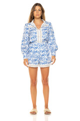 Young woman in blue and white floral romper with lace trim. Long brown hair, tanned skin. Full-body shot against white background. Wearing slide sandals