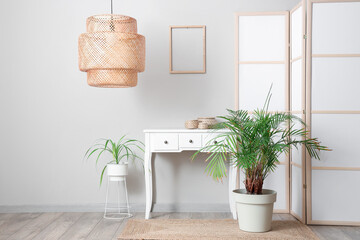 Interior of room with folding screen, commode and houseplants near white wall