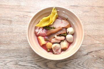 boiled fish ball with dumpling topping slice pickled squid and morning glory in red sauce soup on bowl