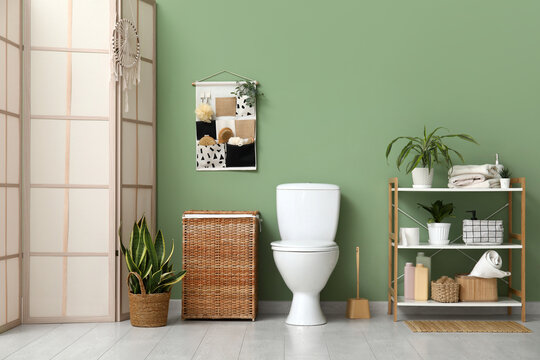 Toilet bowl, shelving unit, laundry basket and organizer on green wall in restroom