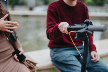 Naklejka premium Two individuals interact next to an electric scooter in a city environment, suggesting modern urban lifestyle and mobility. One person holds a smart phone, highlighting technology use and