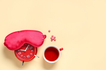 Sleep mask, pills, alarm clock and cup of tea on beige background