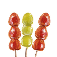 Three skewers of traditional candied fruit, featuring two sticks of glossy, sugar-coated strawberries and shiny green grapes. The caramelized coating creates a vibrant and reflective surface