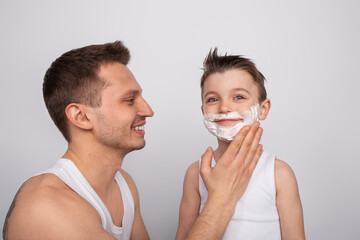 A father helps his young son playfully apply shaving foam to his face, creating a warm bond and...