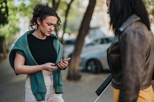 A young woman looks concerned while using her phone on a street, with another person standing nearby. The scene is set in a bright, outdoor urban environment.