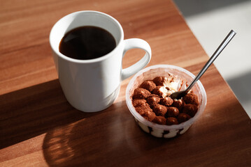 Tiramisu cake and a cup of hot black coffee on a dark wooden table, a fork nearby. Close-up.
