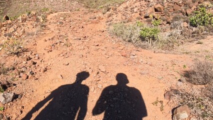 steiniger Pfad in sonnendurchflutetem idyllischem Tal auf Lanzarote mit Schatten von Wanderer,...