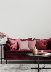 A burgundy velvet sofa with pink pillows sits on a gray rug in front of a white wall