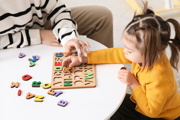 Cute little girl with teacher and letter board learning alphabet at home