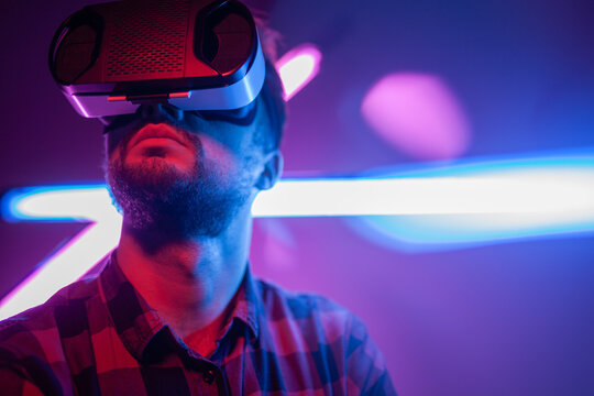 A young man experiencing virtual reality wearing VR goggles, surrounded by vibrant neon lights.