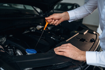 Man is checking engine oil level with a dipstick under the car hood