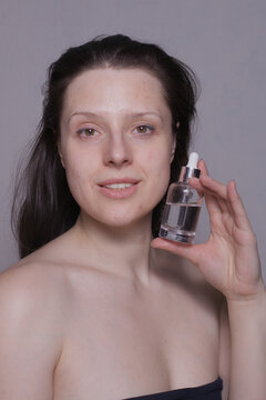 Unedited image of a woman with natural skin holding a transparent serum bottle