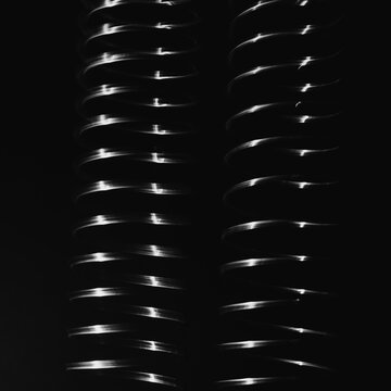Abstract pattern, light shining on a length of fine wire wound around and stretched, against a black background