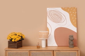 Box with yellow chrysanthemum flowers, lamp and decor on commode near beige wall