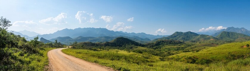 A scenic panoramic view featuring a dirt road winding through lush green hills and mountains under a clear blue sky.