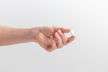 Female hand holding white pill with fingers on white background. Concept of health care, dietary...
