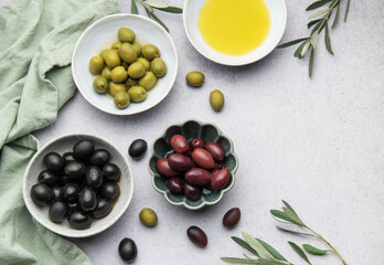 Bowls of black, green and kalamata olives with olive oil and olive branches on marble table