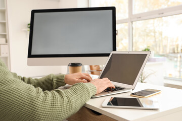 Young man working with blank laptop at table in office, closeup