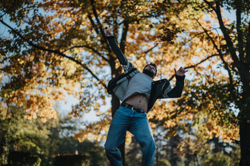 A man leaps with excitement under colorful autumn leaves in a forest. The photo captures movement, freedom, and the beauty of fall with its vivid colors and natural, dynamic atmosphere.