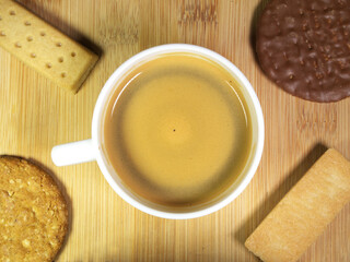 Closeup overhead shot of biscuits surrounding a white cup containing just stirred hot coffee.