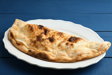 Plate with tasty calzone on blue wooden table, closeup