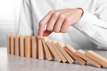 Man stopping wooden blocks from falling at table, closeup. Domino effect