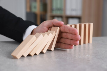 Man stopping wooden blocks from falling at table, closeup. Domino effect