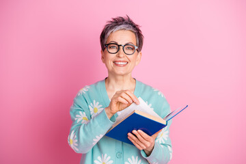 Smiling professional woman holding an open book against pink background, reflecting charm and...