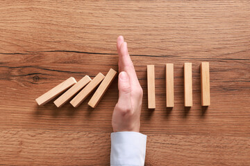 Man stopping wooden blocks from falling at table, top view. Domino effect