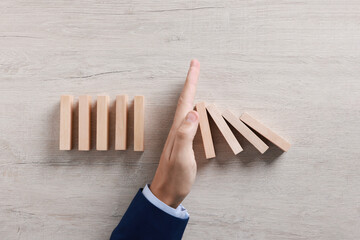 Man stopping wooden blocks from falling at table, top view. Domino effect