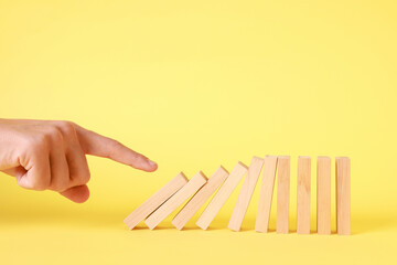 Domino effect. Man pushing wooden blocks on yellow background, closeup