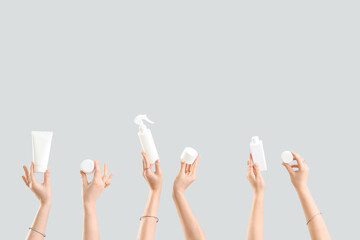 Many female hands with bottles and jars of cosmetic products on grey background
