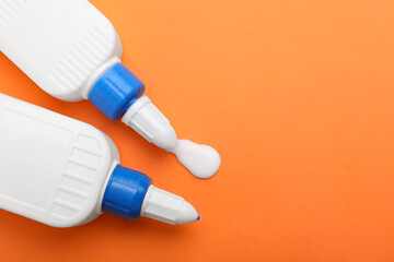 Bottles of glue on orange background, top view. Space for text