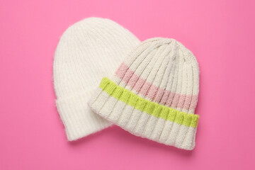 Warm woolen hats on pink background, top view