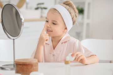 Cute little happy girl in pajamas with mirror applying cream at home