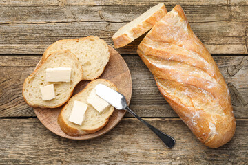 Slices of fresh baguette with butter on wooden table, flat lay