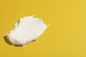 Cream on dark yellow background, closeup. Sample of cosmetic product